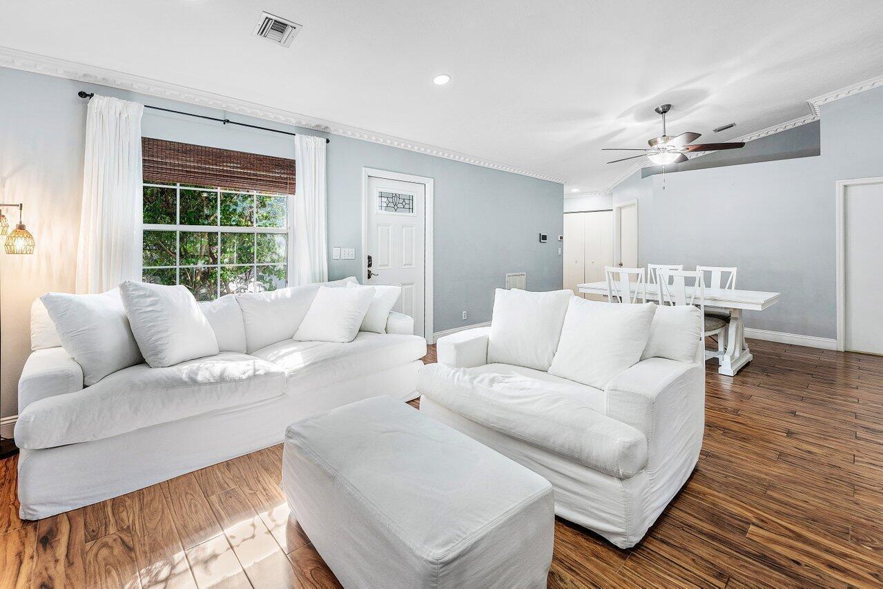 A living room with white sofas, a matching ottoman, and a dining area on hardwood floors — 5418 Club Circle, Haverhill FL 33415, HAVERHILL, FL