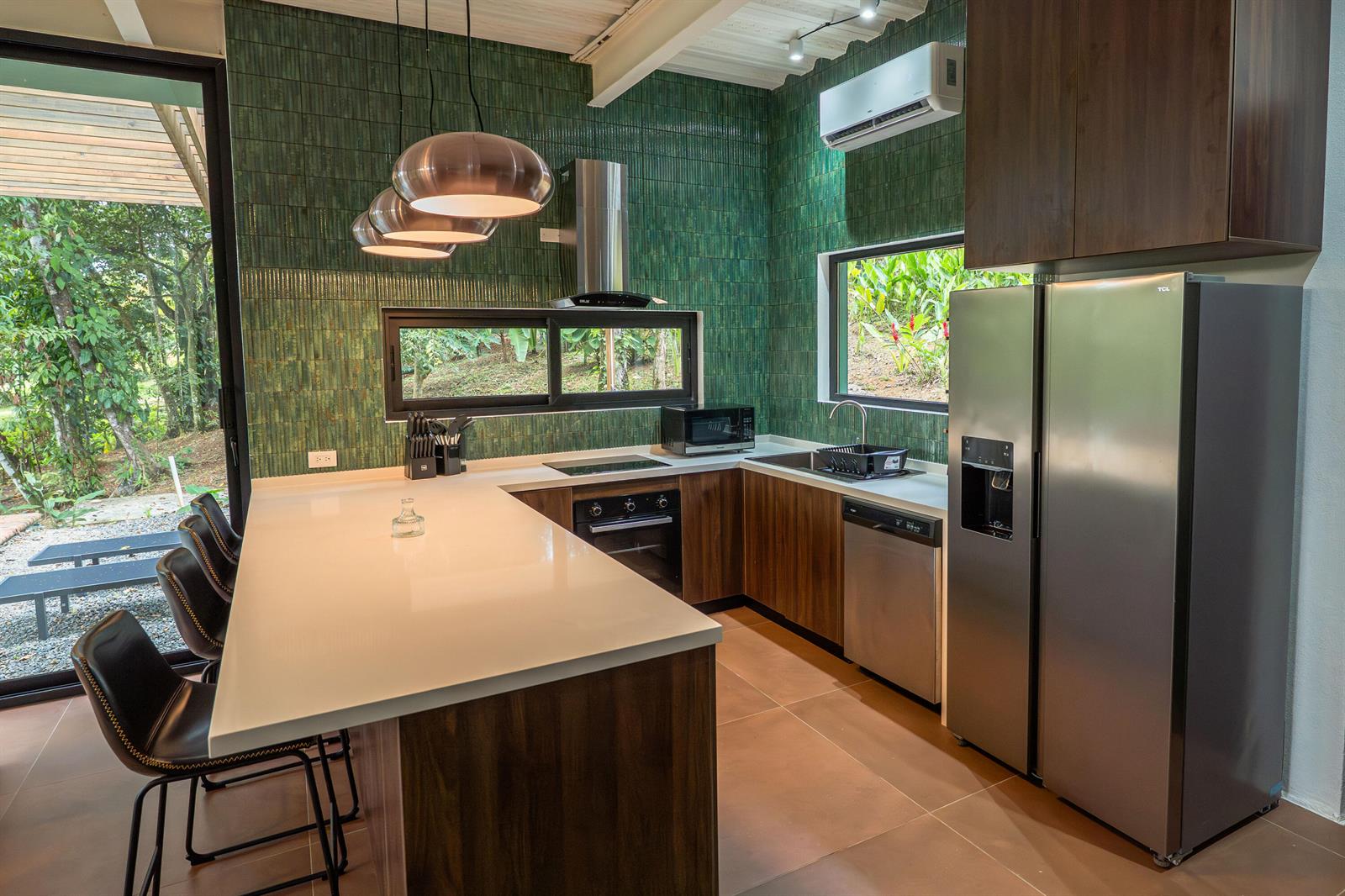 A modern kitchen features green tiled walls, wood cabinetry, a white island, and stainless appliances — 200 Burn Brae Way, Bocas Del Toro,, FL