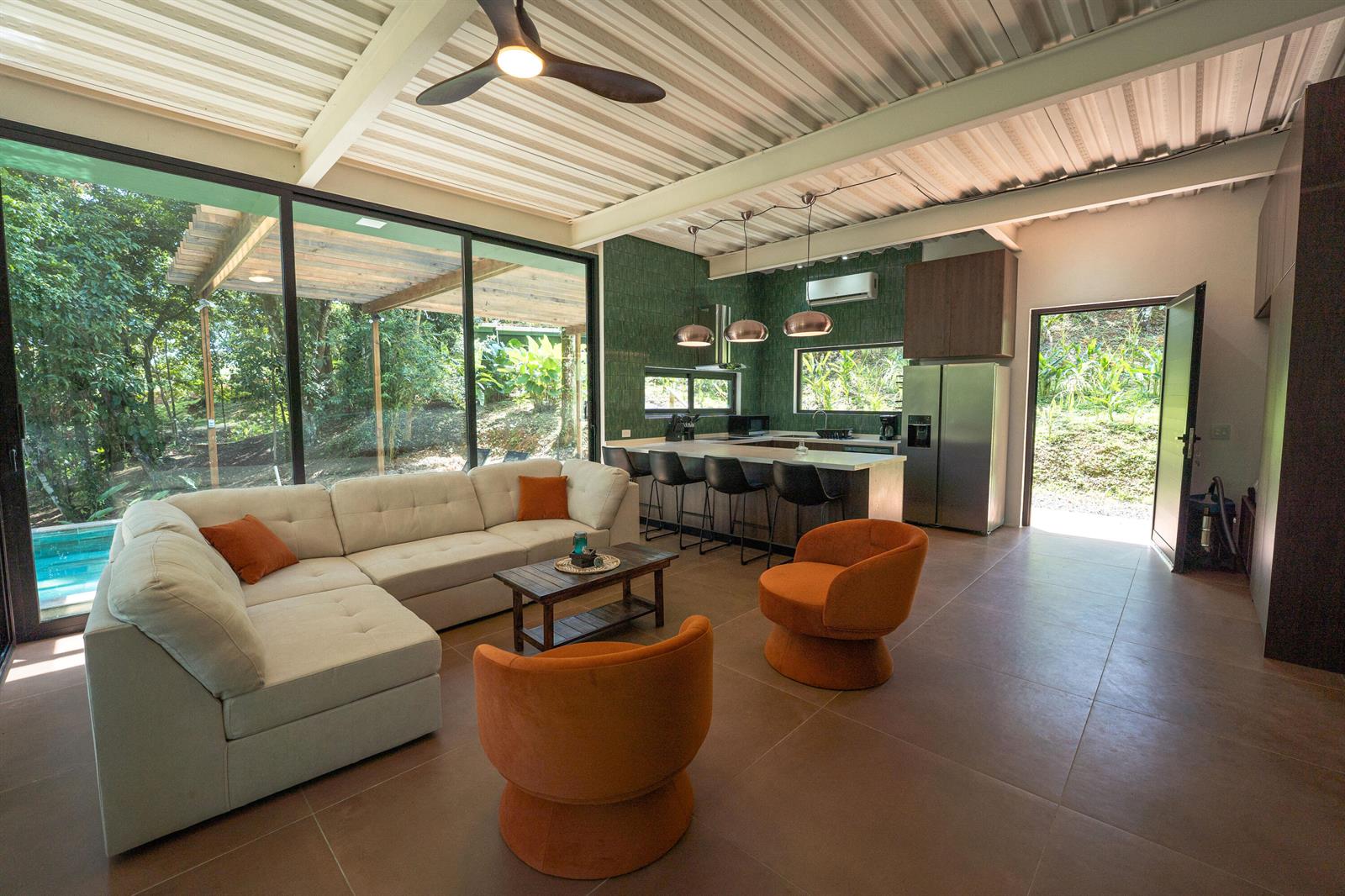 An open-concept living room and kitchen featuring a sectional sofa, orange chairs, and floor-to-ceiling windows — 200 Burn Brae Way, Bocas Del Toro,, FL