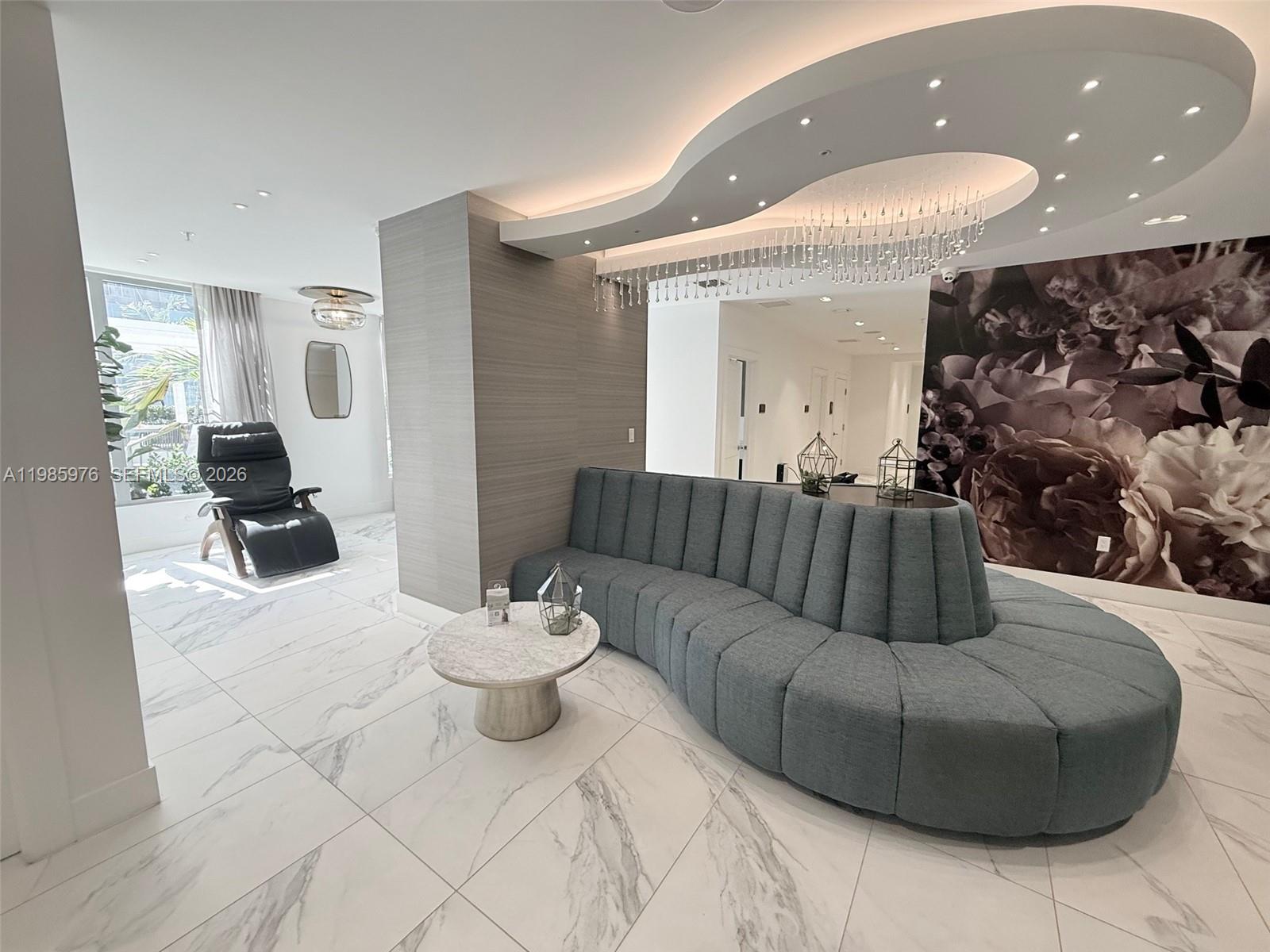 A modern lounge area features a curved blue sofa, marble flooring, and a floral wall — 218 NW 8th St, Miami FL 33136, MIAMI, FL