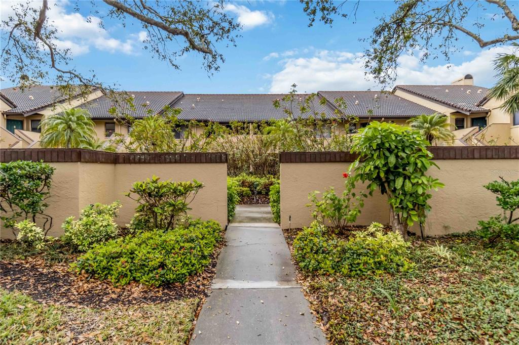 A concrete walkway leads through a low wall toward a two-story residential building with landscaping — 5734 ASHTON LAKE DRIVE UNIT 7, SARASOTA, FL