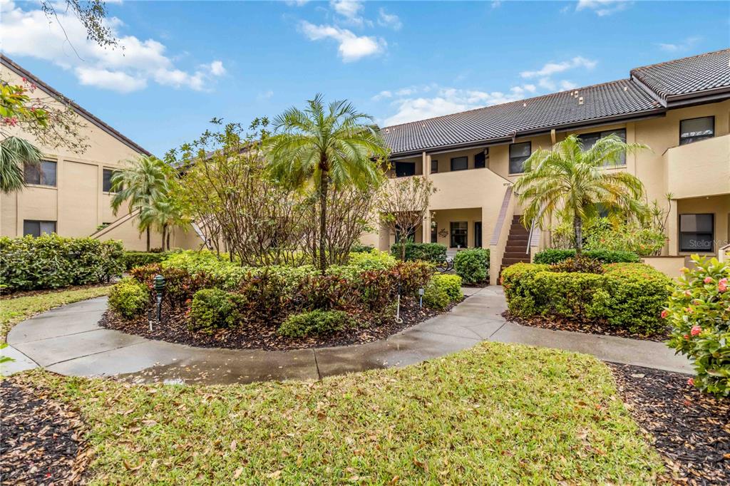 A paved walkway curves through a landscaped courtyard between two-story tan apartment buildings — 5734 ASHTON LAKE DRIVE UNIT 7, SARASOTA, FL