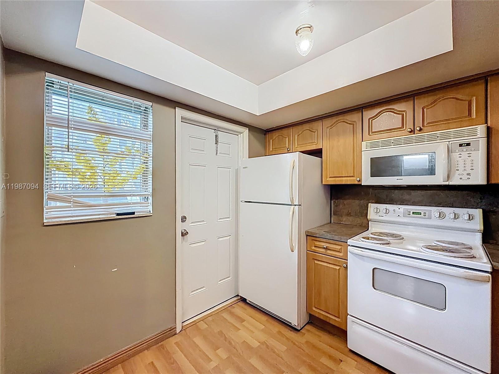 A kitchen features light wood cabinets, white appliances, a white door, and a window — 6730 Arbor Dr # 110, Miramar FL 33023, MIRAMAR, FL