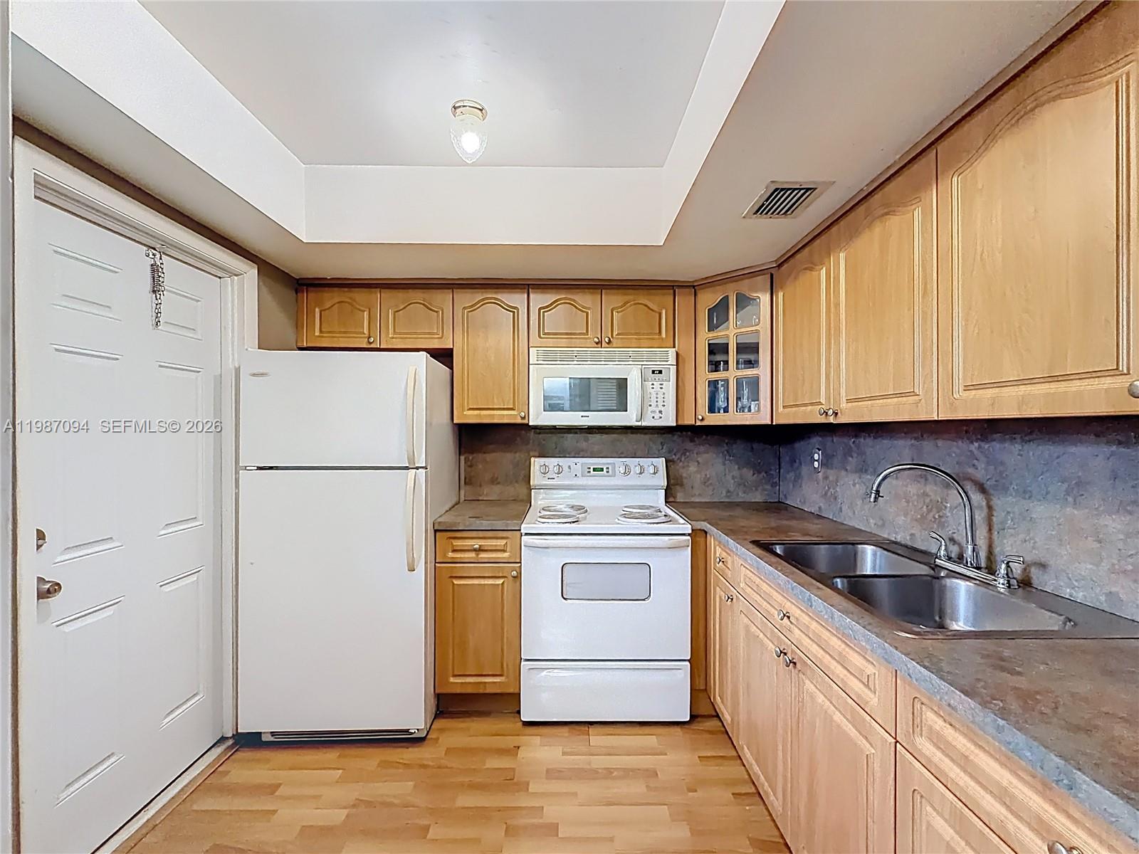 A kitchen features light wood cabinets, white appliances, a double sink, and wood-look flooring — 6730 Arbor Dr # 110, Miramar FL 33023, MIRAMAR, FL
