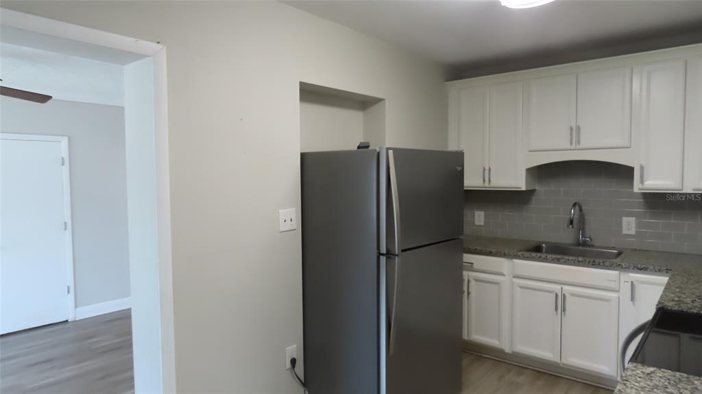 A kitchen features white cabinets, gray subway tile backsplash, granite countertops, and a stainless refrigerator — 6543 34TH TERRACE N, ST PETERSBURG, FL