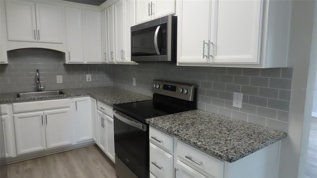 A kitchen features white cabinets, granite countertops, a stainless steel microwave, and gray subway tile — 6543 34TH TERRACE N, ST PETERSBURG, FL