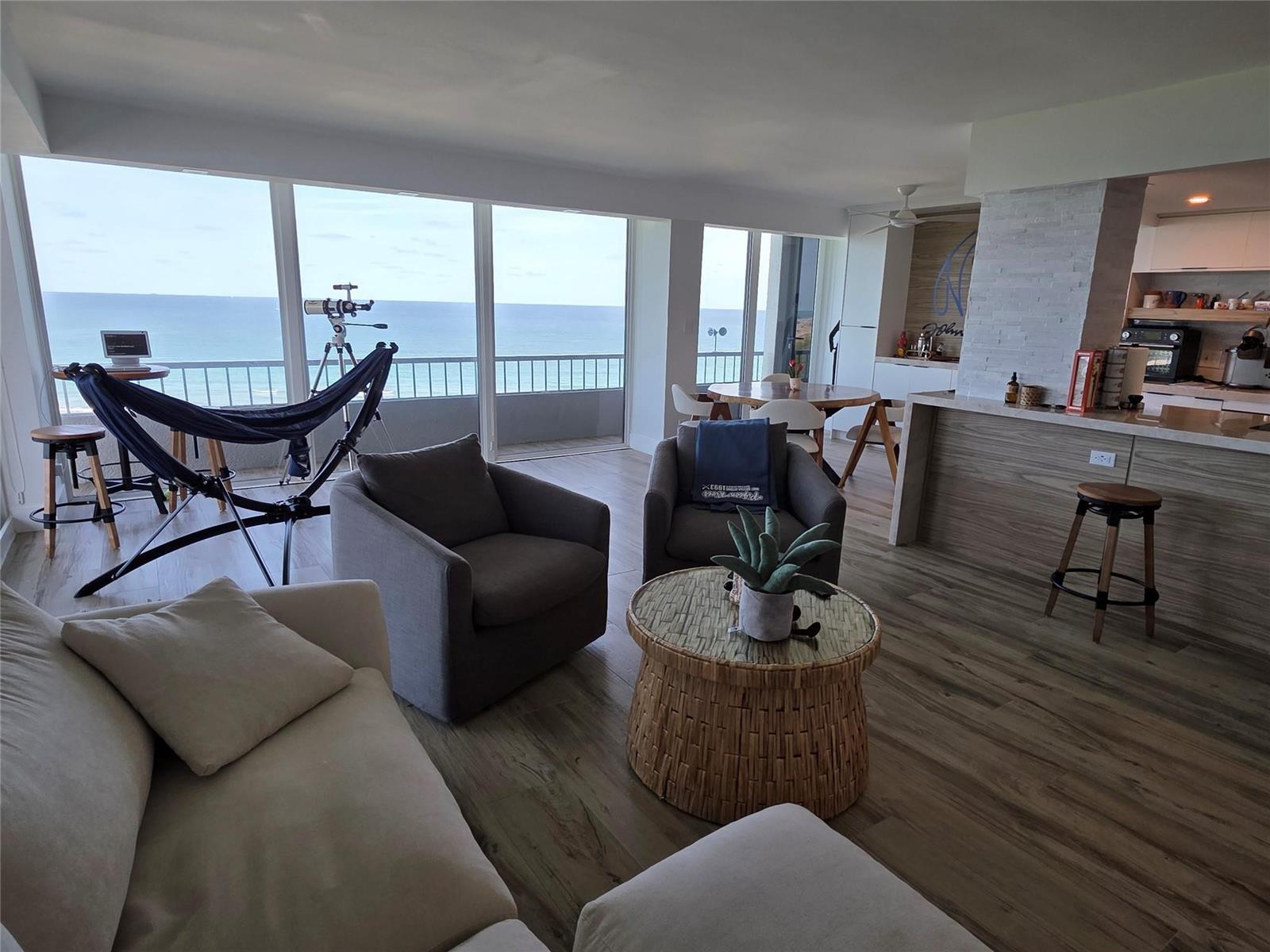 An open-concept living room features a balcony with ocean views, wood flooring, and a kitchen — 5550 N Ocean Drive, Riviera Beach FL 33404, RIVIERA BEACH, FL