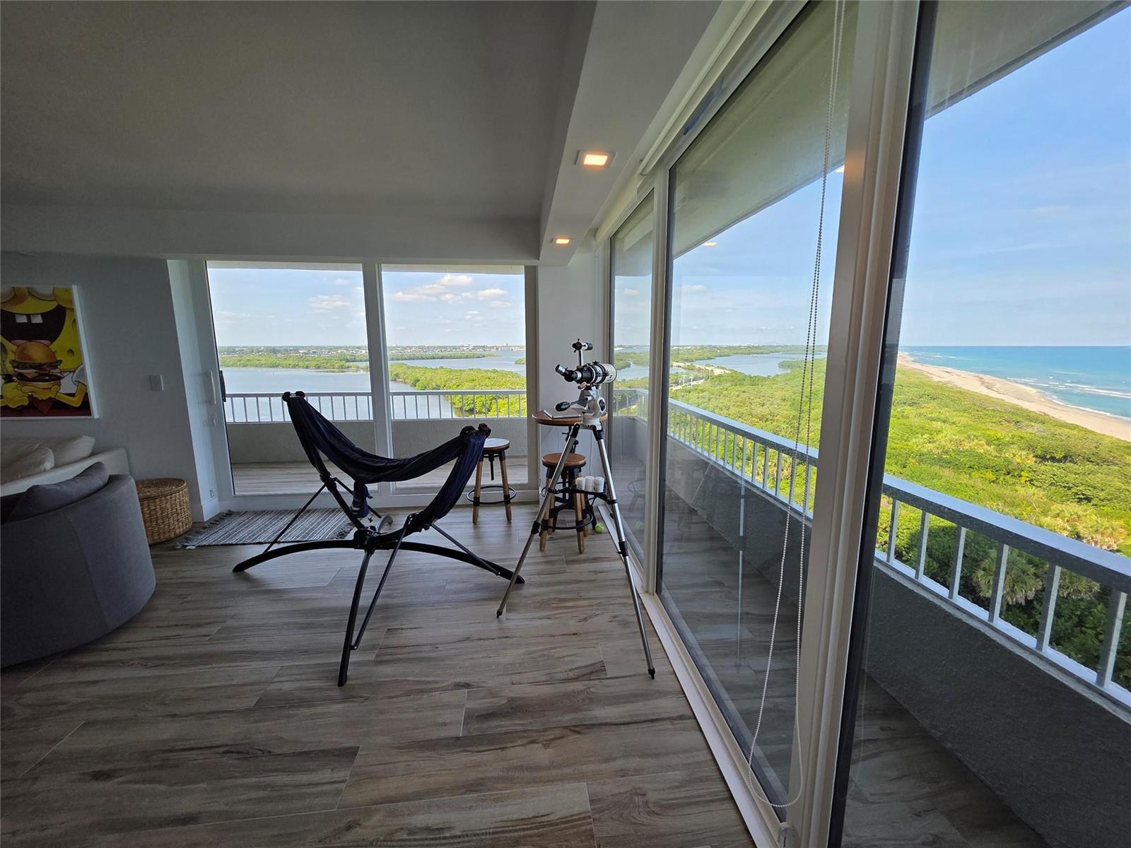 A living room with wood-look flooring, a hammock chair, a telescope, and a balcony view — 5550 N Ocean Drive, Riviera Beach FL 33404, RIVIERA BEACH, FL