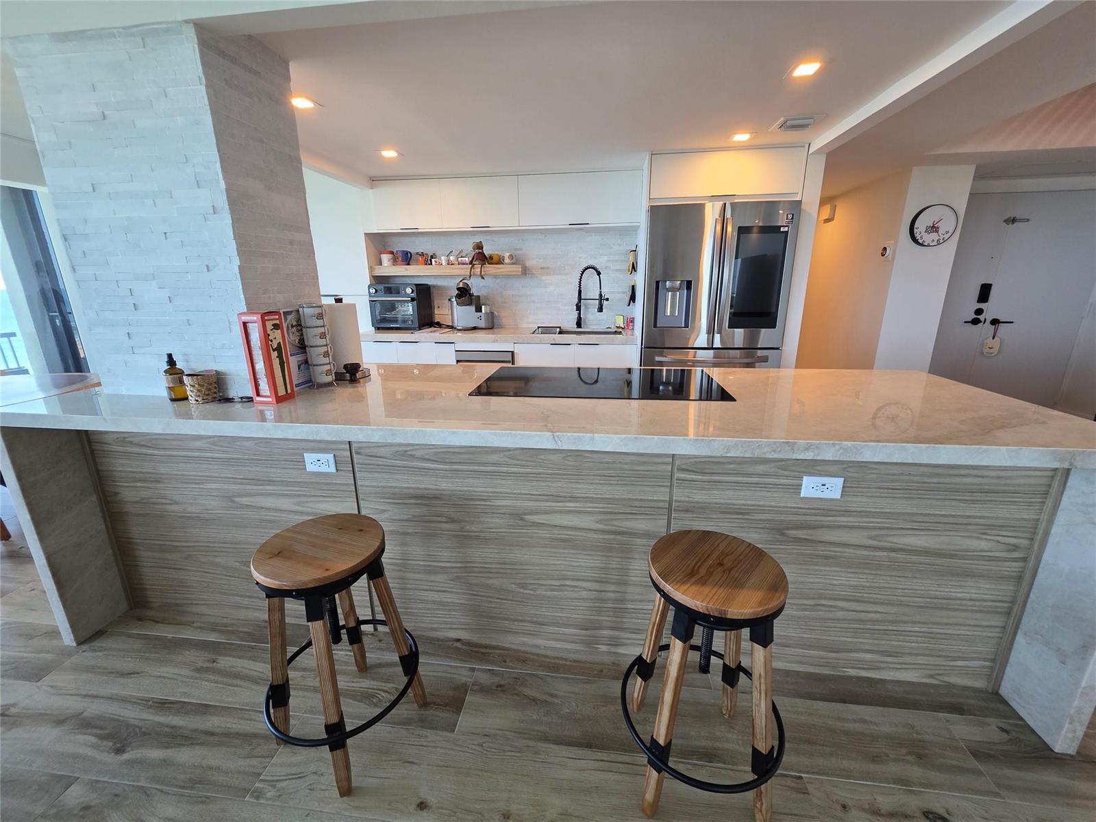 A kitchen features a large island with a cooktop, wood-grain cabinetry, and two bar stools — 5550 N Ocean Drive, Riviera Beach FL 33404, RIVIERA BEACH, FL