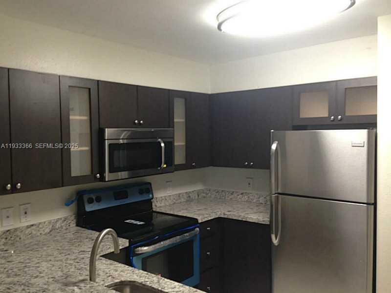A kitchen features dark wood cabinets, stainless steel appliances, and speckled granite countertops — 4350 NW 107th Ave # 102, Doral FL 33178, DORAL, FL