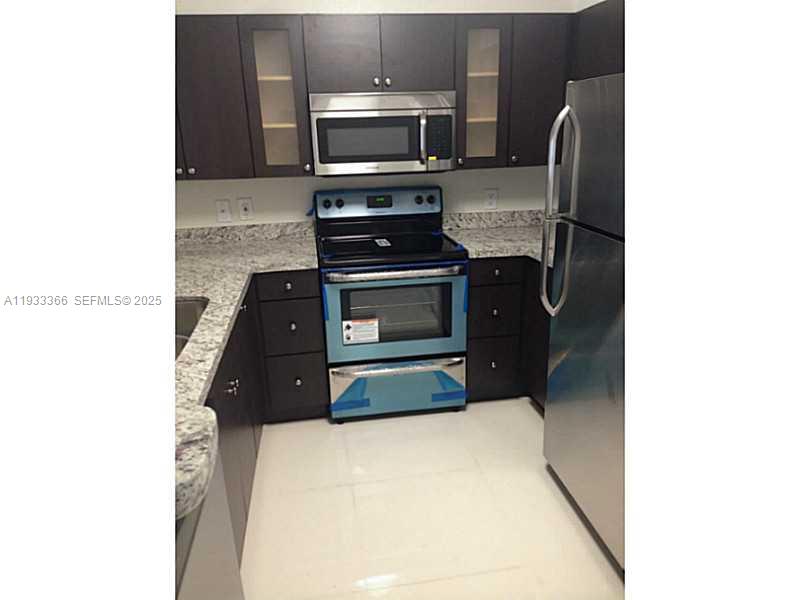 A kitchen features dark wood cabinets, granite countertops, and stainless steel appliances — 4350 NW 107th Ave # 102, Doral FL 33178, DORAL, FL