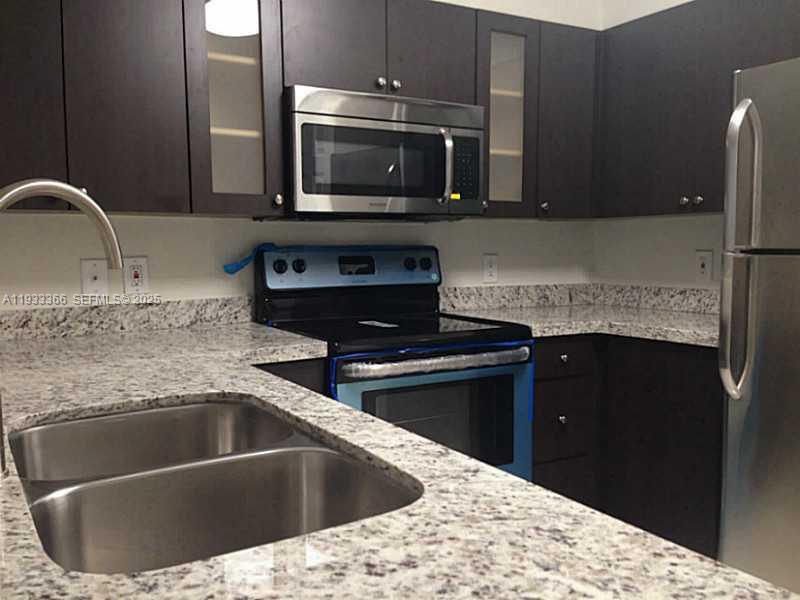 A kitchen features dark wood cabinets, granite countertops, stainless steel appliances, and a double-basin sink — 4350 NW 107th Ave # 102, Doral FL 33178, DORAL, FL