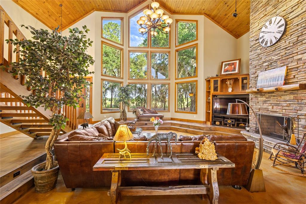 A rustic living room features a stone fireplace, vaulted wood ceiling, and large floor-to-ceiling windows — 10925 ARROWTREE BOULEVARD, CLERMONT, FL