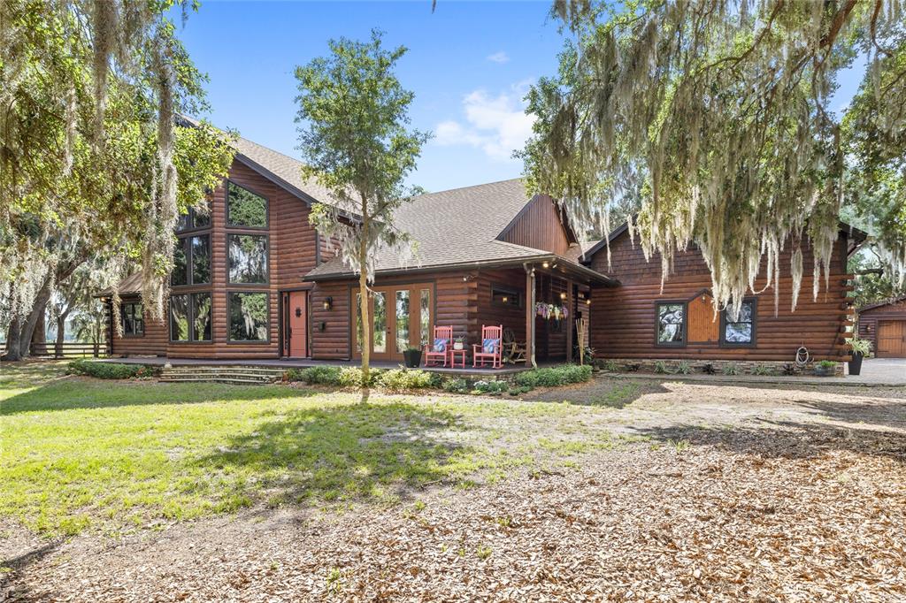 A large, two-story log cabin home features a covered porch and surrounding oak trees — 10925 ARROWTREE BOULEVARD, CLERMONT, FL