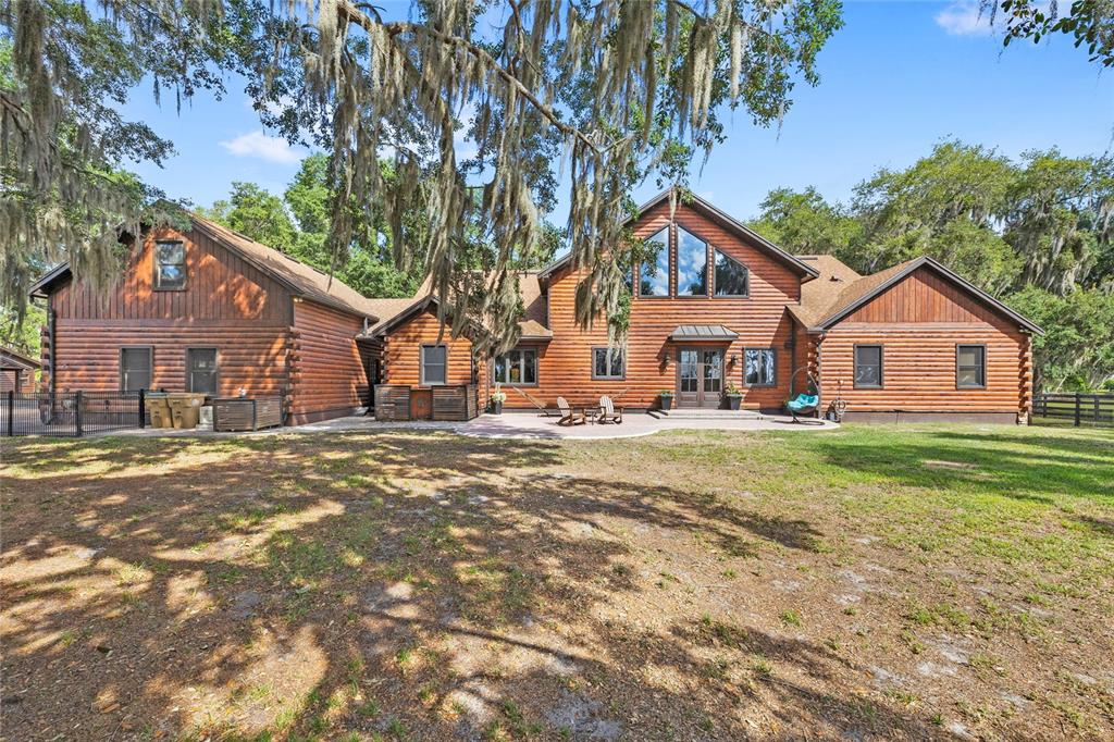 A large, two-story log cabin home features a stone patio and surrounding oak trees — 10925 ARROWTREE BOULEVARD, CLERMONT, FL