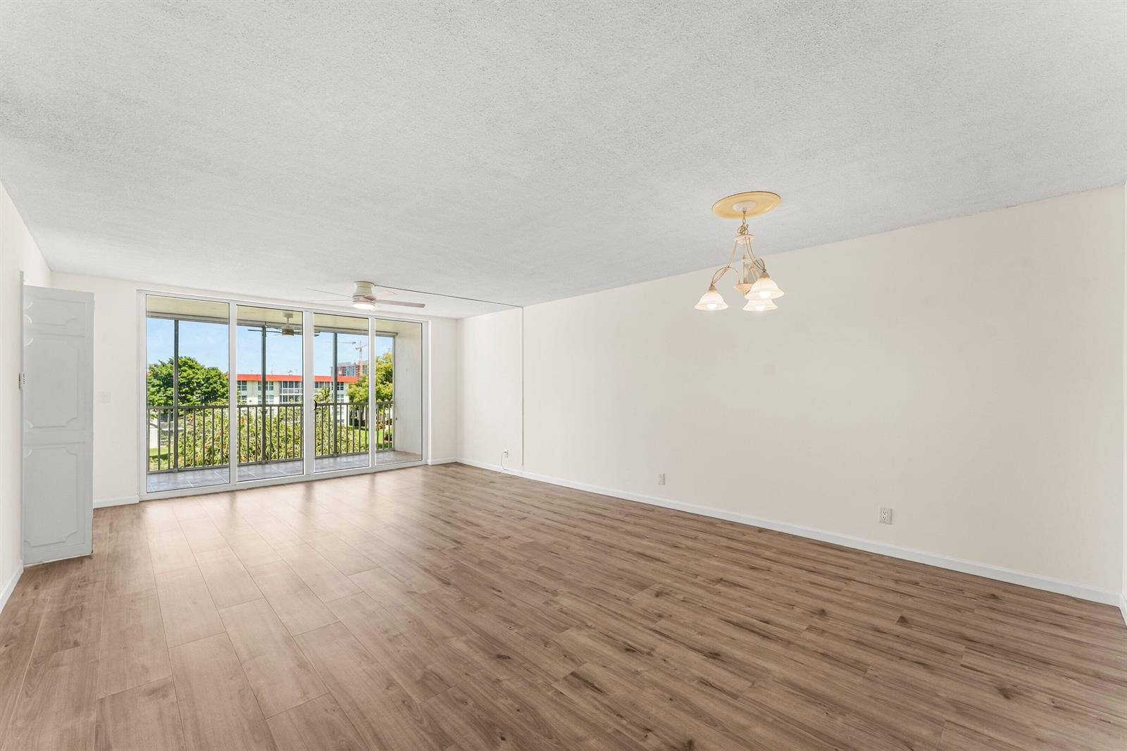 An empty living room with wood-look flooring, a ceiling fan, and a sliding glass door — 3100 NE 48th Court # 415, Lighthouse Point FL 33064, LIGHTHOUSE POINT, FL