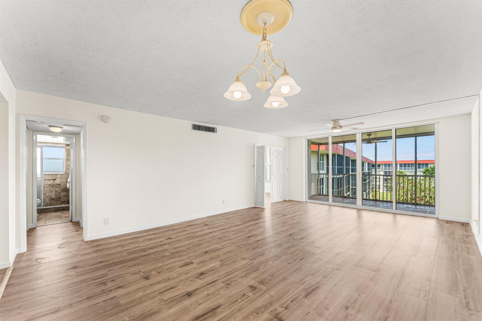 An empty living room with wood-look flooring, a chandelier, and sliding glass doors to a balcony — 3100 NE 48th Court # 415, Lighthouse Point FL 33064, LIGHTHOUSE POINT, FL