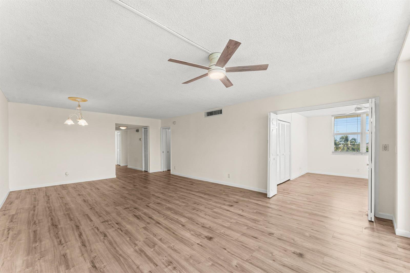 An empty living room features light wood-look flooring, a ceiling fan, and an adjacent bedroom — 3100 NE 48th Court # 415, Lighthouse Point FL 33064, LIGHTHOUSE POINT, FL