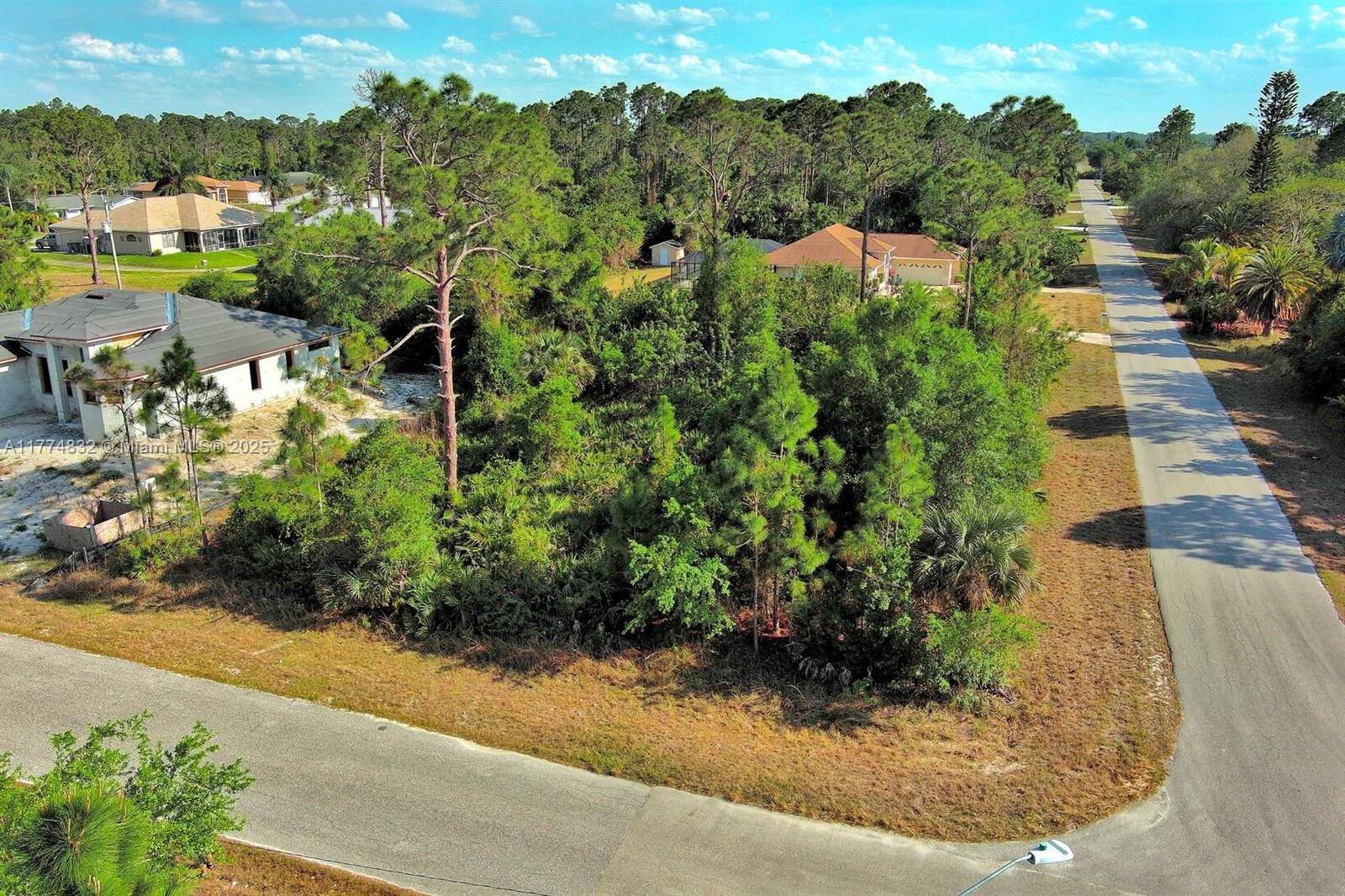 An aerial view shows a vacant, wooded residential lot situated between two houses and roads — 2500 E 9th St, Lehigh Acres FL 33936, LEHIGH ACRES, FL
