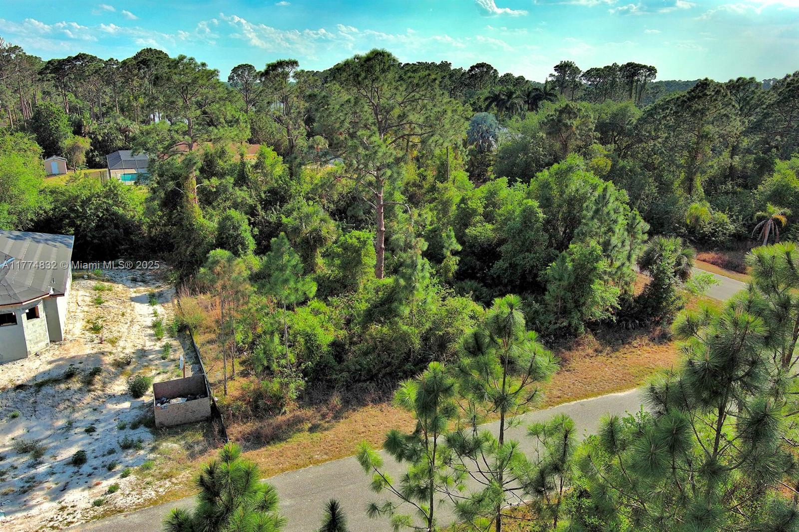 An aerial view shows a wooded lot next to a house under construction and road — 2500 E 9th St, Lehigh Acres FL 33936, LEHIGH ACRES, FL