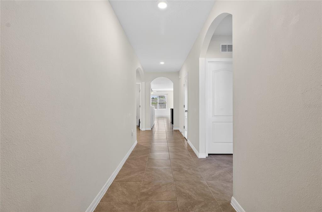A long hallway with beige walls, tile flooring, and arched doorways leads to a window — 2658 GRANDBURY GROVE ROAD, LAKELAND, FL