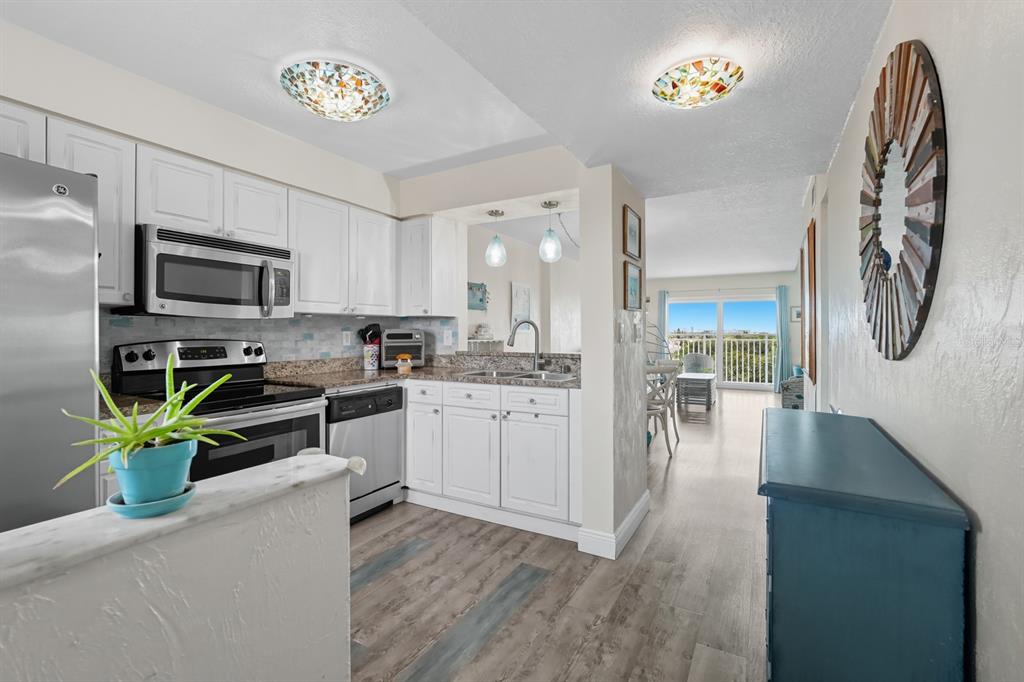 A kitchen with white cabinets and stainless steel appliances opens to a bright living area — 145 N HALIFAX UNIT 704, DAYTONA BEACH, FL