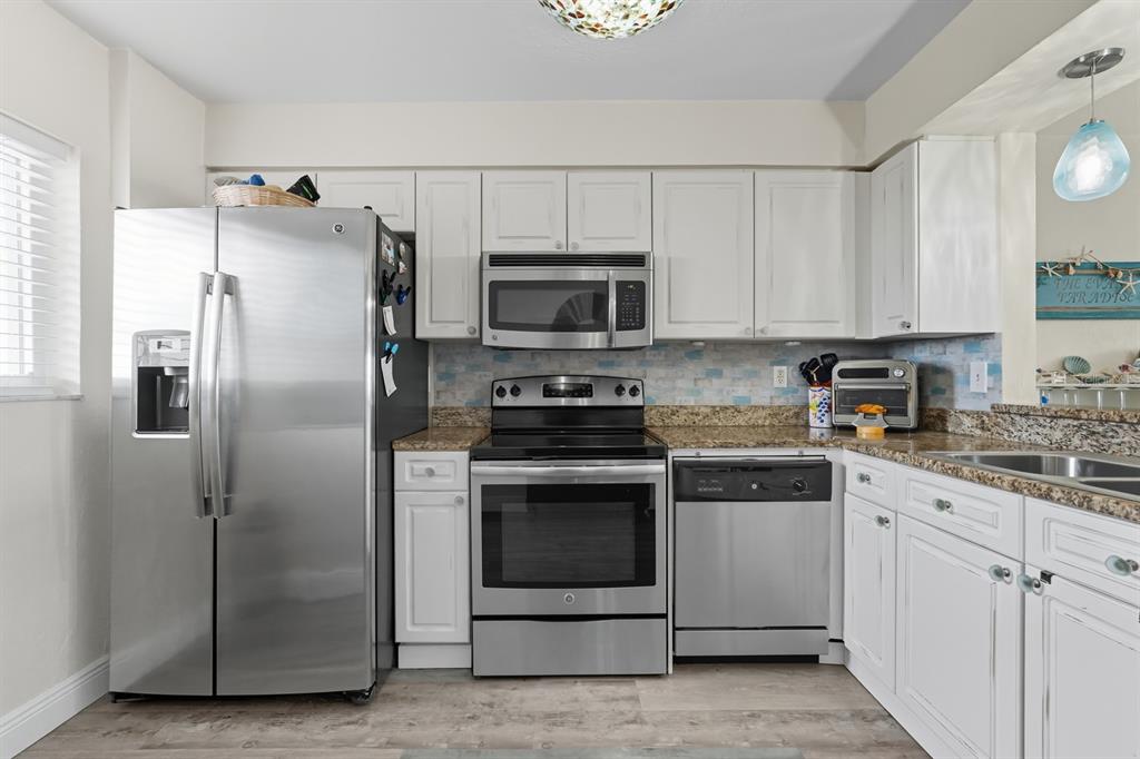 A kitchen with white cabinets, stainless steel appliances, granite countertops, and a blue tile backsplash — 145 N HALIFAX UNIT 704, DAYTONA BEACH, FL