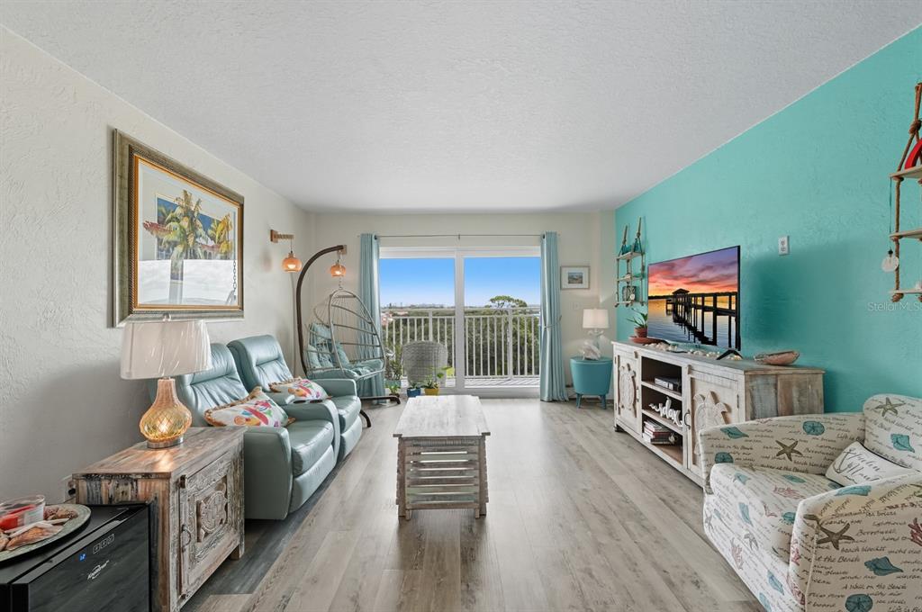 A living room features light wood flooring, a teal accent wall, and a balcony view — 145 N HALIFAX UNIT 704, DAYTONA BEACH, FL