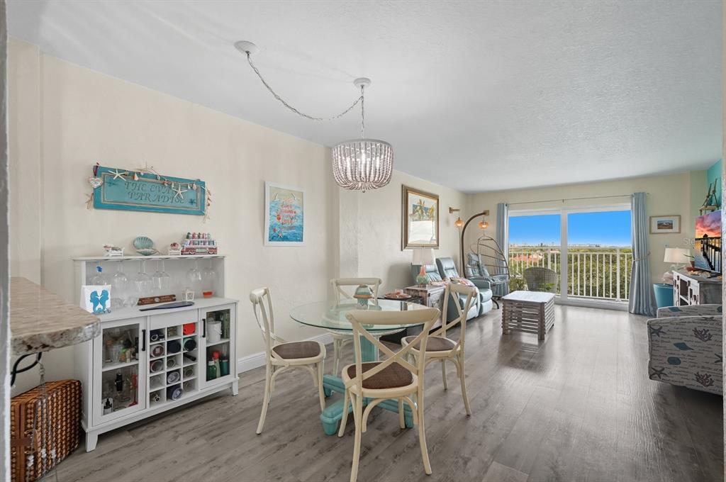 A dining area and living room with wood-look flooring, a glass table, and a balcony view — 145 N HALIFAX UNIT 704, DAYTONA BEACH, FL