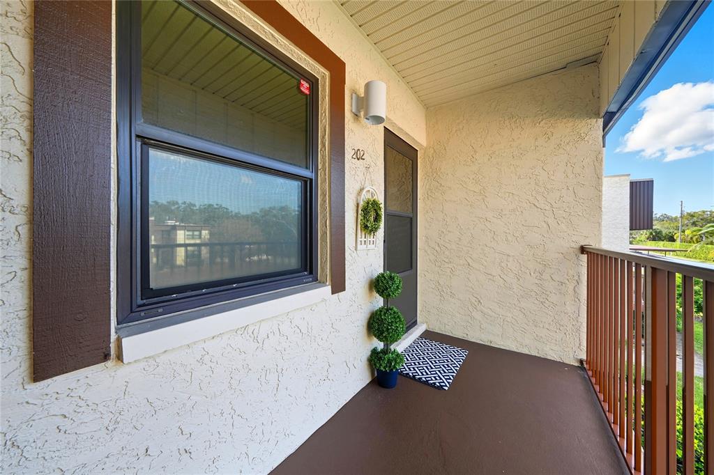 A covered balcony features a dark brown floor, a window, and a front door — 2400 WINDING CREEK BOULEVARD UNIT 9-202, CLEARWATER, FL