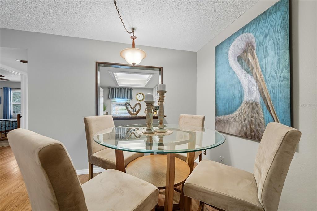 A dining room features a glass-topped table, four beige chairs, and a large pelican wall art — 2400 WINDING CREEK BOULEVARD UNIT 9-202, CLEARWATER, FL