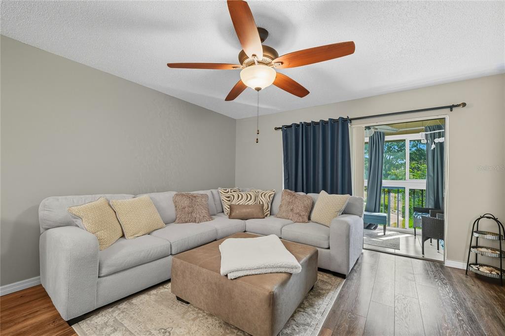 A living room features a gray sectional sofa, a leather ottoman, and a sliding glass door — 2400 WINDING CREEK BOULEVARD UNIT 9-202, CLEARWATER, FL