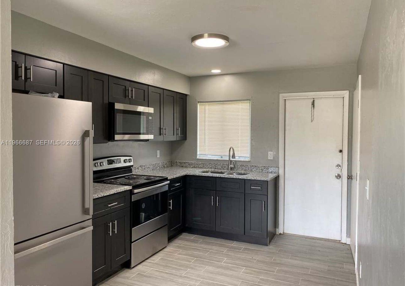 A kitchen features dark cabinets, stainless steel appliances, granite countertops, and light wood-look flooring — 132/134 S Gordon, Lehigh Acres FL 33973, LEHIGH ACRES, FL