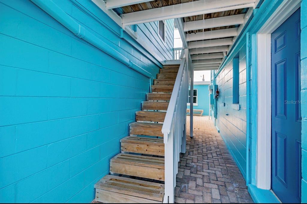 An outdoor wooden staircase leads up between two bright blue walls on a paved walkway — 13343 GULF BOULEVARD UNIT 14, MADEIRA BEACH, FL