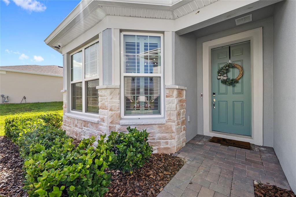 The exterior of a house features a teal front door, stone accents, and a window — 5196 FOOTHILLS PRESERVE LOOP, MOUNT DORA, FL