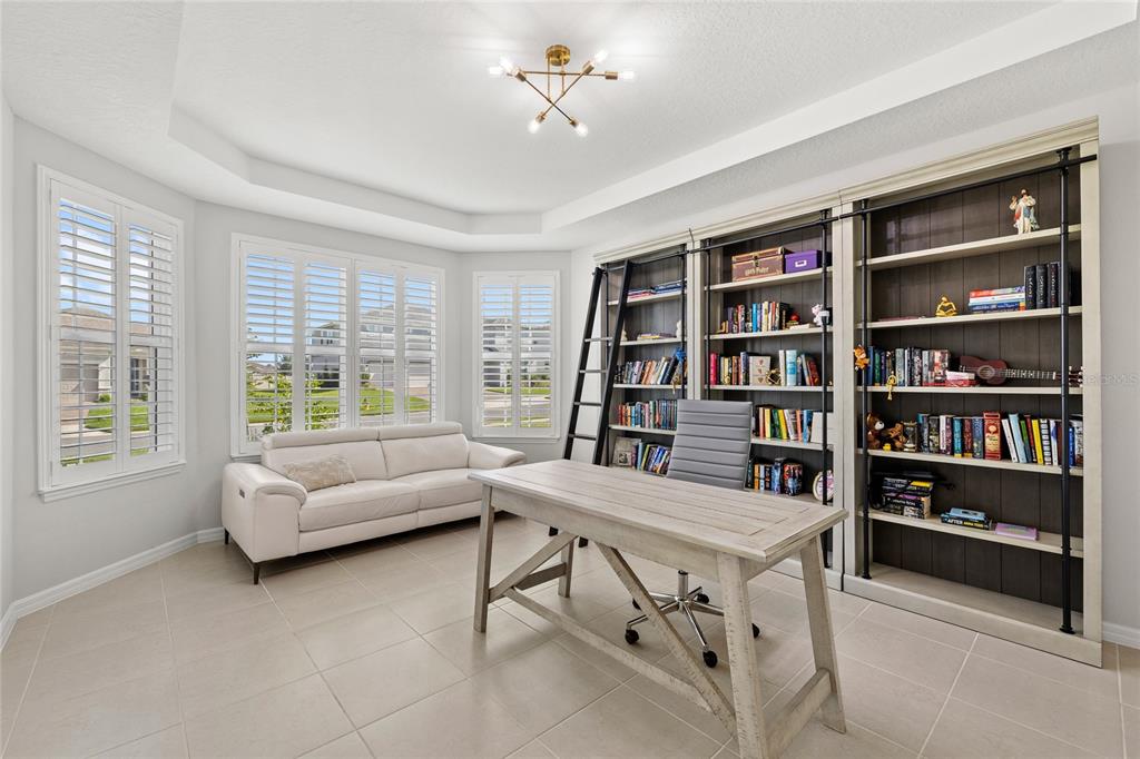 A home office features a desk, a white sofa, and floor-to-ceiling bookshelves with a ladder — 5196 FOOTHILLS PRESERVE LOOP, MOUNT DORA, FL