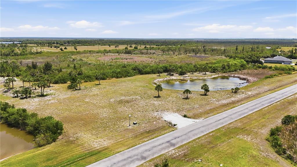 An aerial view shows a vacant grassy lot with a small pond and paved road — 11610 BRIDLE PATH LANE, PLACIDA, FL