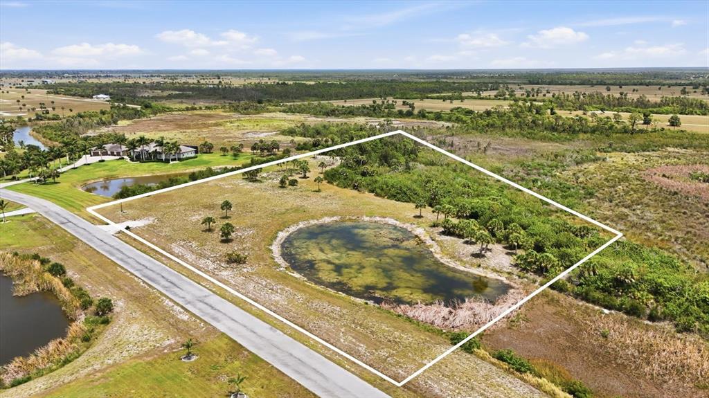 An aerial view shows a vacant, grassy lot with a pond and surrounding vegetation — 11610 BRIDLE PATH LANE, PLACIDA, FL