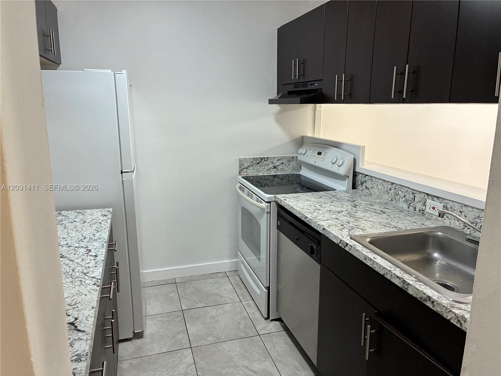 A kitchen features dark cabinets, granite countertops, white appliances, and light-colored floor tiles — 10801 SW 109th Ct # D203, Miami FL 33176, MIAMI, FL