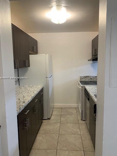 A galley kitchen features dark wood cabinets, granite countertops, white appliances, and light tile flooring — 10801 SW 109th Ct # D203, Miami FL 33176, MIAMI, FL