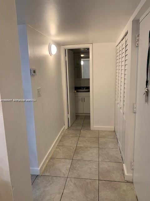 A hallway with light-colored tile flooring leads to a bathroom with a vanity and mirror — 10801 SW 109th Ct # D203, Miami FL 33176, MIAMI, FL