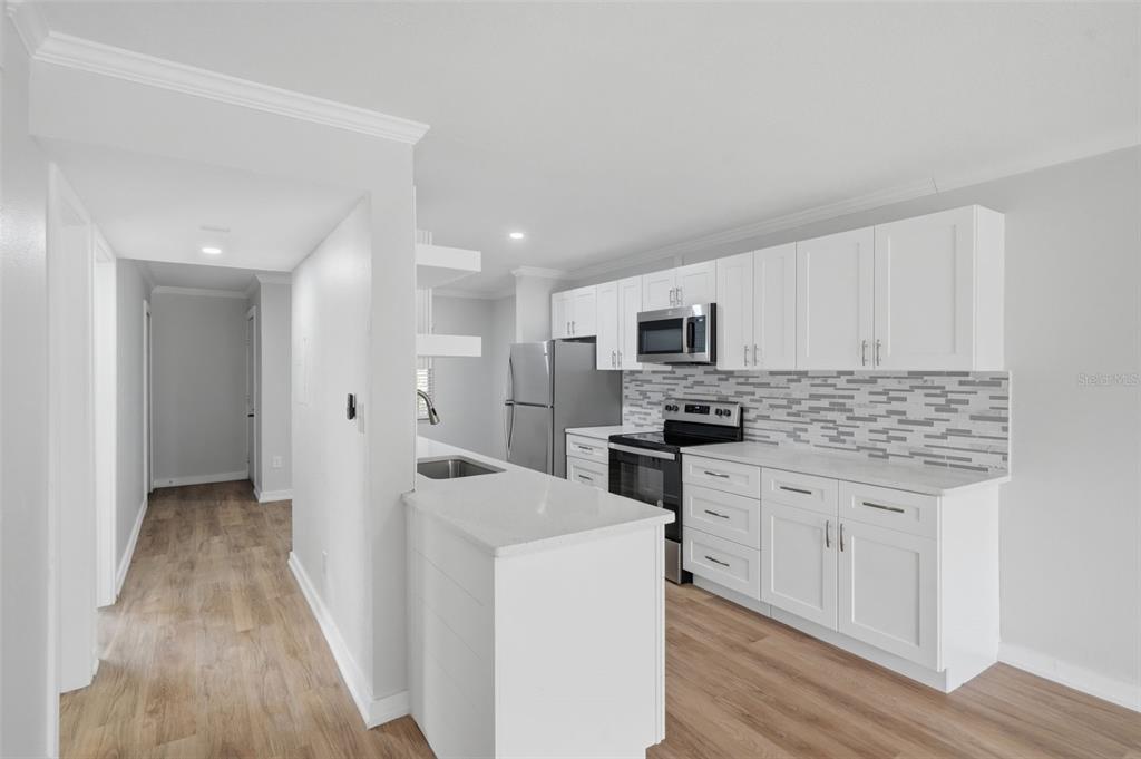 A modern kitchen features white cabinets, stainless steel appliances, and a light-colored quartz countertop — 11201 122ND AVENUE UNIT 116, LARGO, FL