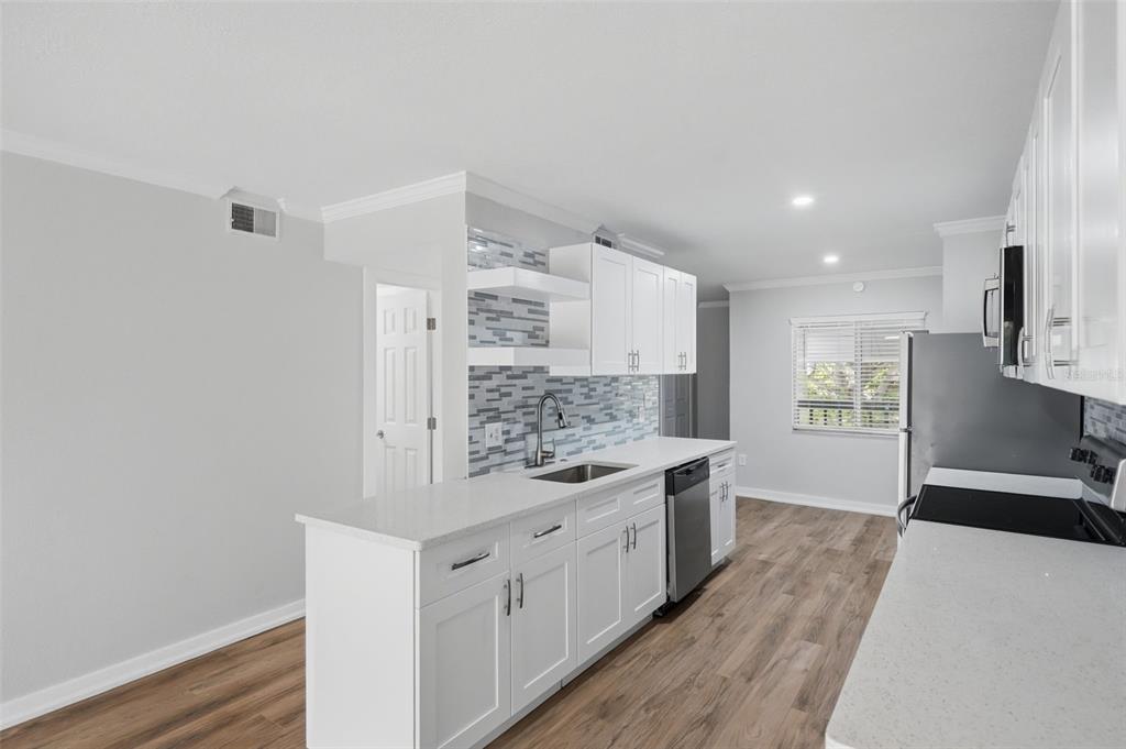 A modern kitchen features white cabinets, quartz countertops, a tile backsplash, and light wood flooring — 11201 122ND AVENUE UNIT 116, LARGO, FL