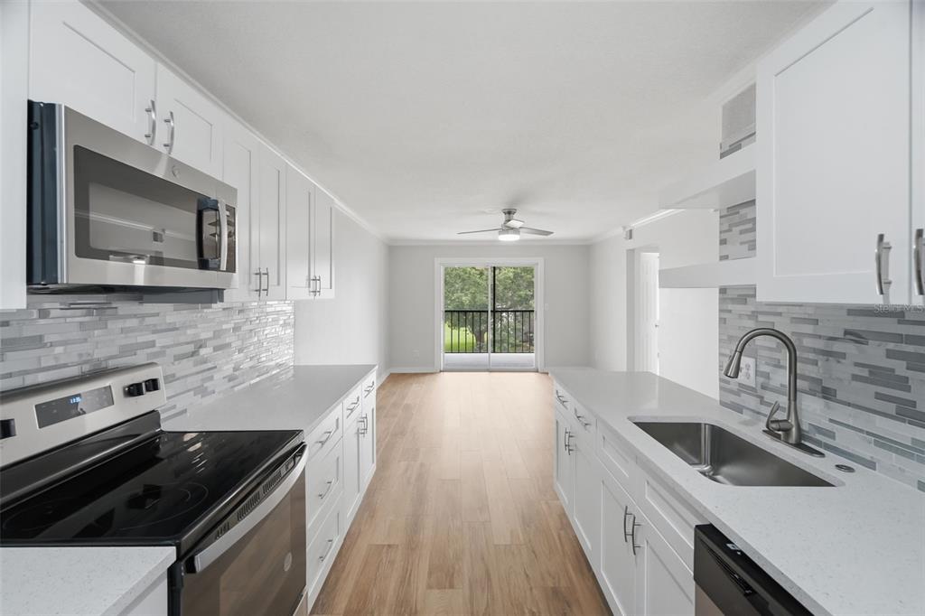 A galley kitchen features white cabinets, stainless steel appliances, and a view of a balcony — 11201 122ND AVENUE UNIT 116, LARGO, FL