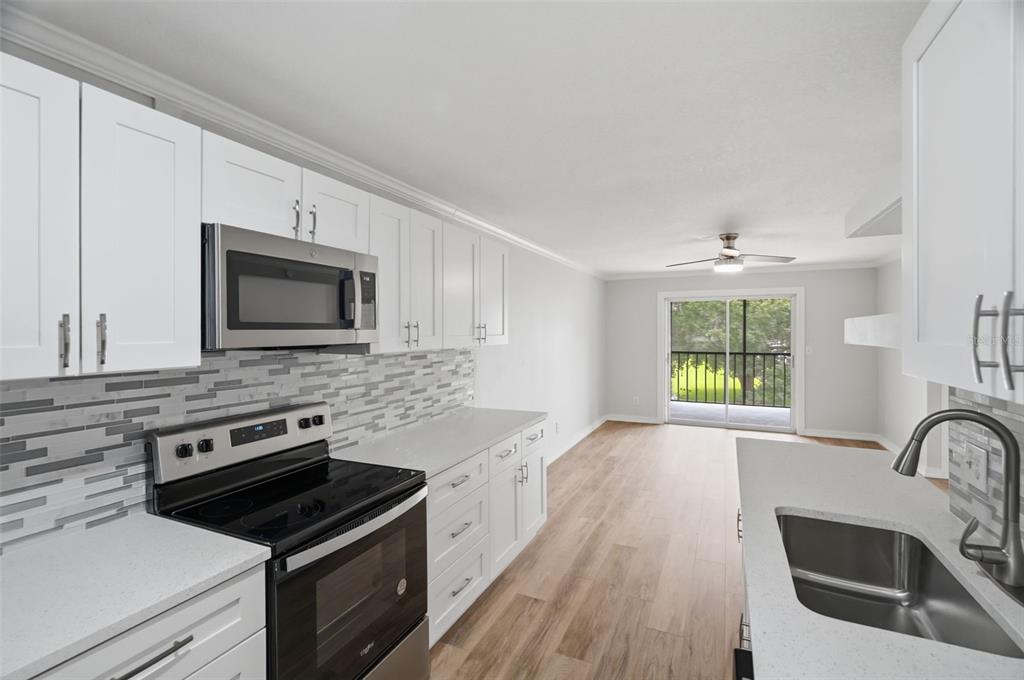 A kitchen with white cabinets, stainless steel appliances, and a view of a balcony — 11201 122ND AVENUE UNIT 116, LARGO, FL