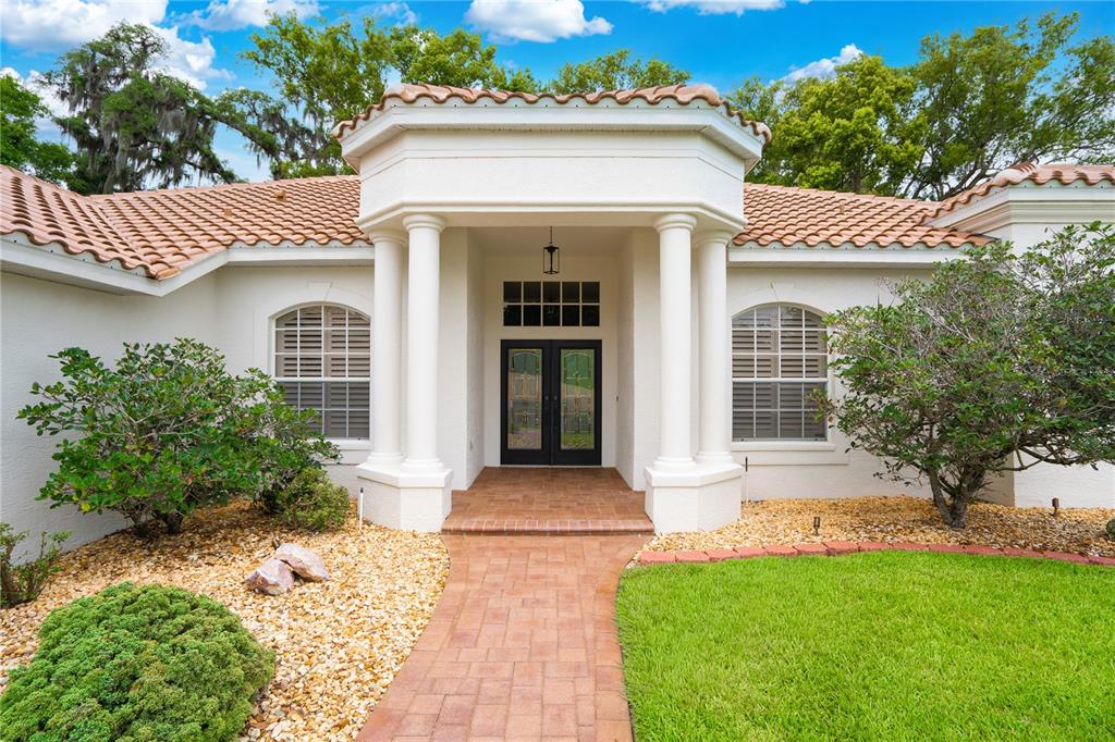 A white house with a tiled roof, columns, and a brick walkway leading to the entrance — 12649 OAK HOLLOW COURT, DADE CITY, FL