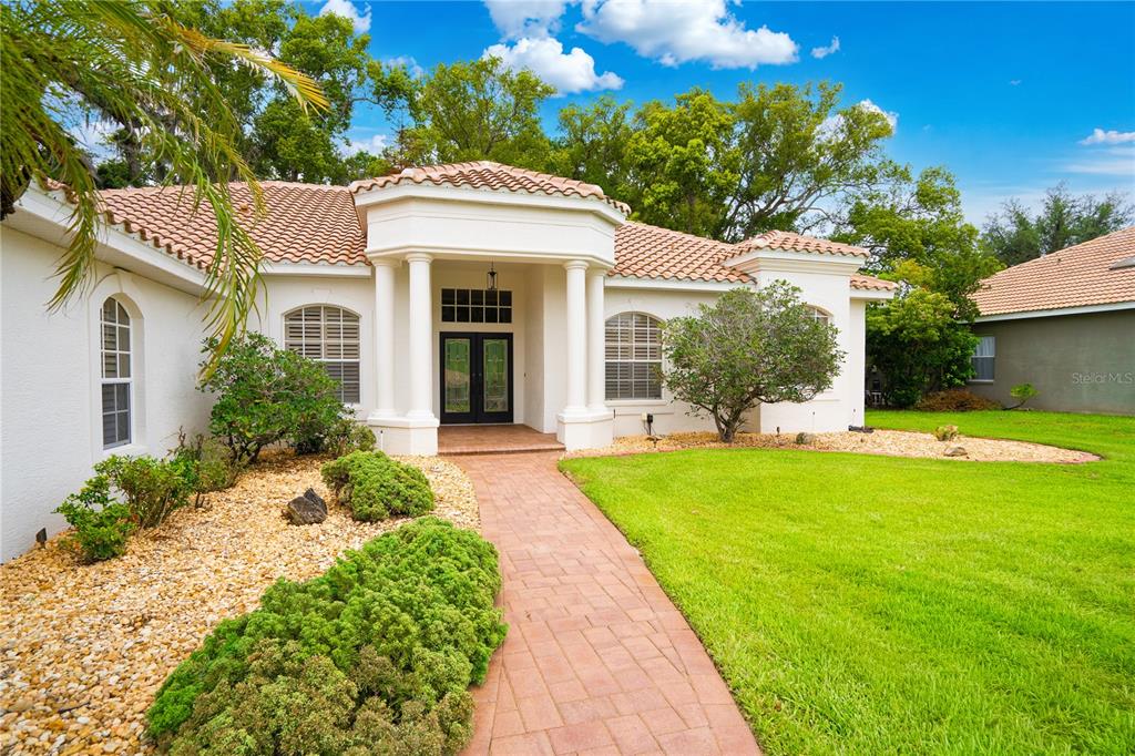 A single-story house with a tiled roof, white stucco exterior, and a brick walkway entrance — 12649 OAK HOLLOW COURT, DADE CITY, FL