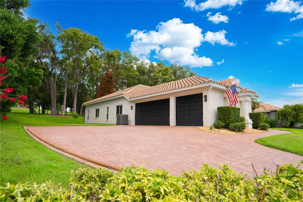 A house exterior featuring a two-car garage, a brick paver driveway, and a tiled roof — 12649 OAK HOLLOW COURT, DADE CITY, FL