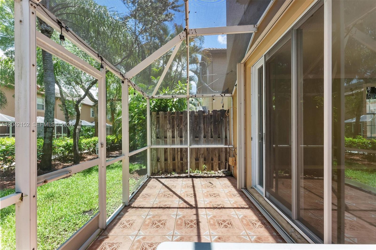 A screened-in patio features tiled flooring, a wooden privacy fence, and sliding glass doors — 1552 Barcelona Way # 19, Weston FL 33327, WESTON, FL