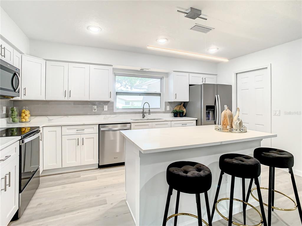 A modern kitchen features white cabinetry, stainless steel appliances, a center island, and bar stools — 2642 BROOKSIDE COURT, MAITLAND, FL